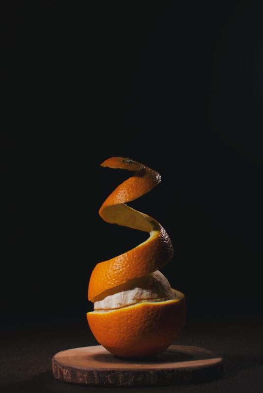 Peeled orange unraveling upward with black background. 