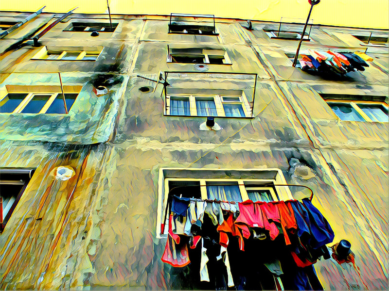 Looking up at a yellow building with bright laundry hanging from its windows. 