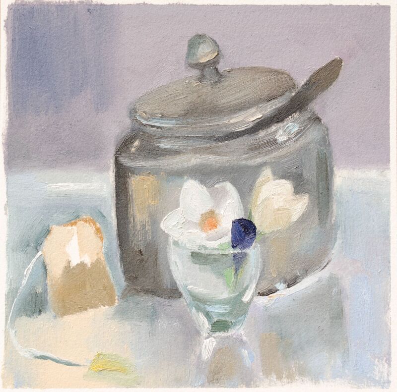 Still life, gray sugar bowl with tilted lid and spoon handle. Foreground is a small clear vase with two white flowers beside and tea bag. 